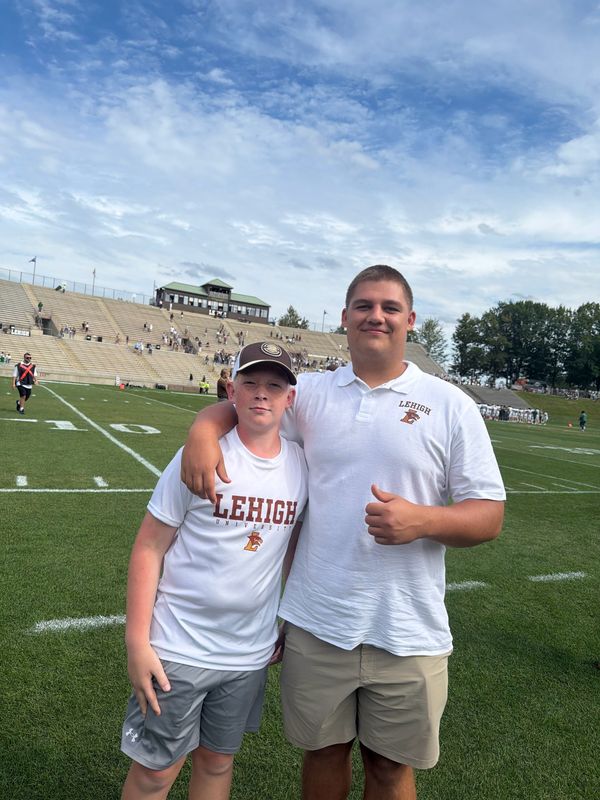 Brothers Jack and Sam Naylon in Lehigh shirts, standing together on a college football field with the stands behind them.